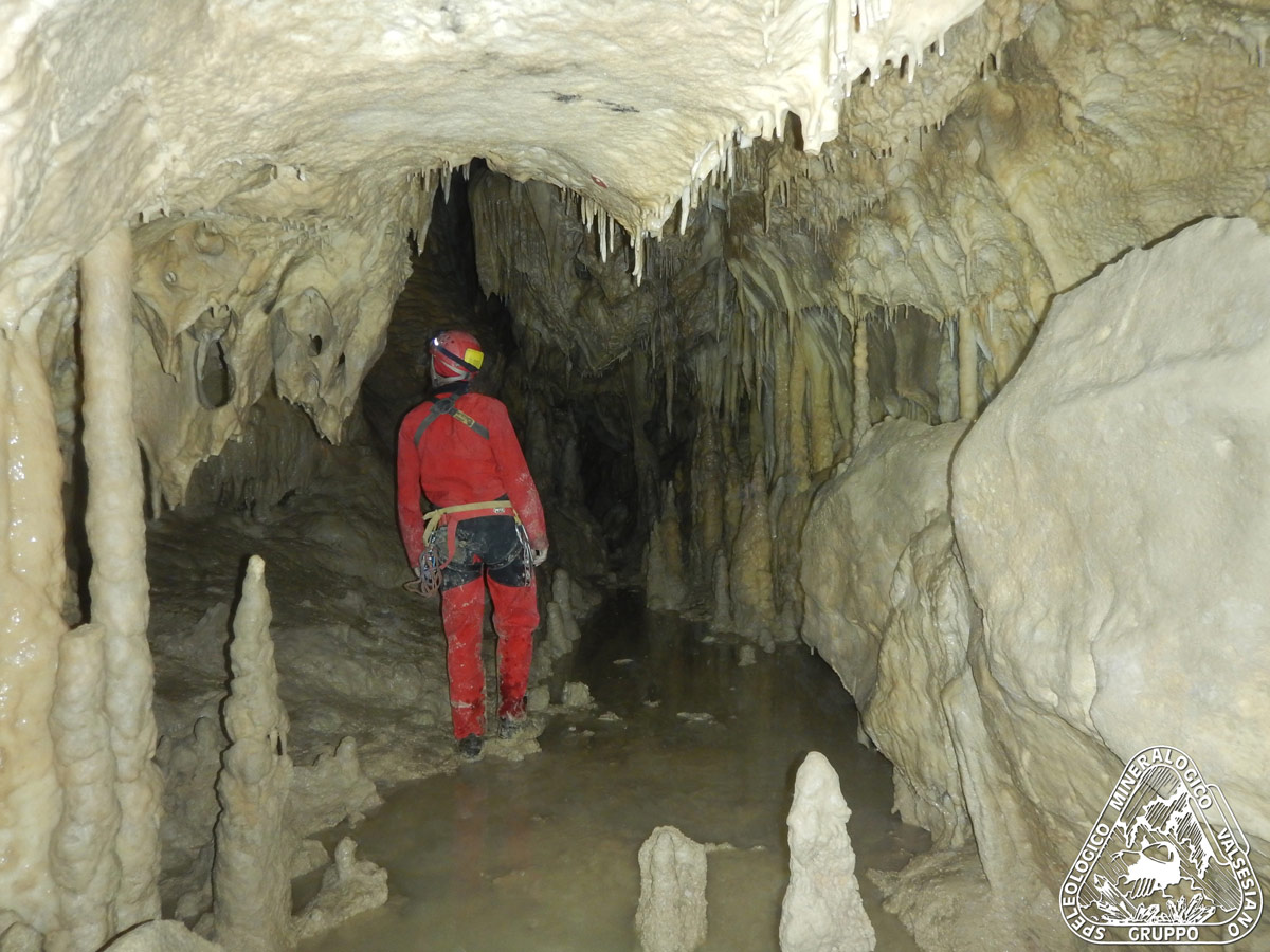 Saletta concrezionata con laghetto nella grotta di Frasassi e speleologo che la sta espolorando; le concrezioni, stalattiti e stalagminti, lo circondano